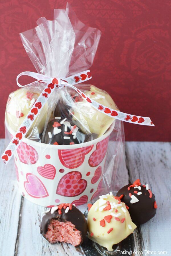 A Valentine's Day Cup filled with cake pops with 3 cake pops laying in front of it. 