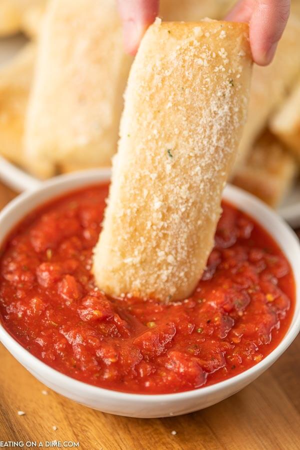 A Little Caesar's Crazy Bread Stick being dipped into a bowl of pizza sauce.  