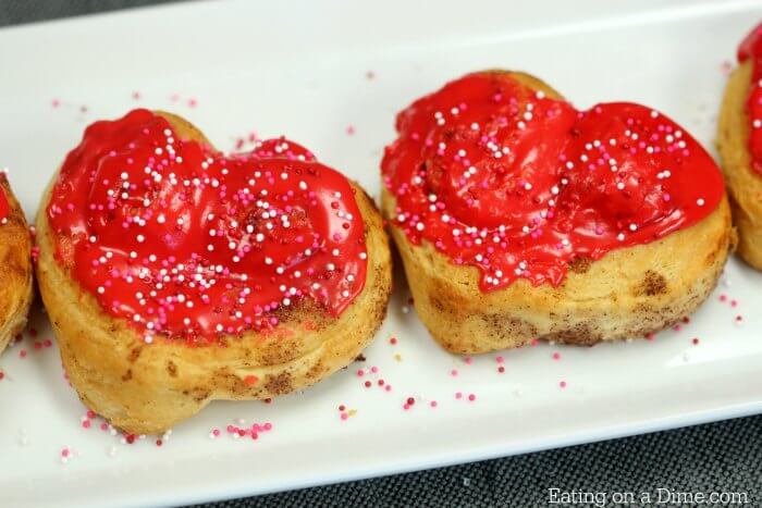 Heart shaped cinnamon rolls topped with red icing and Valentine's Day sprinkles 