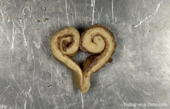 The cinnamon roll dough shaped into a heart on a baking sheet 