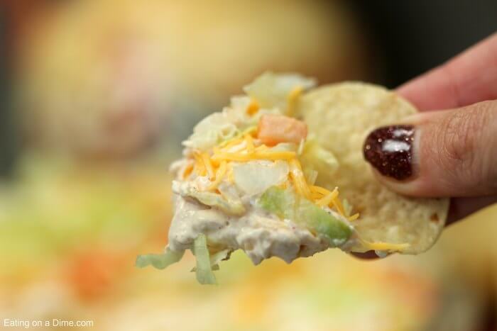 Close up image of Taco Dip in a white dish with a serving on a chip. 