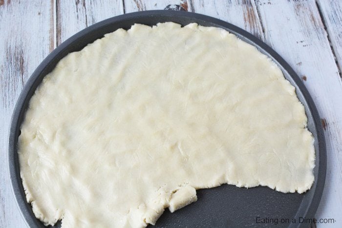 Close up image of the uncooked cookie crust being spread on a pizza pan. 