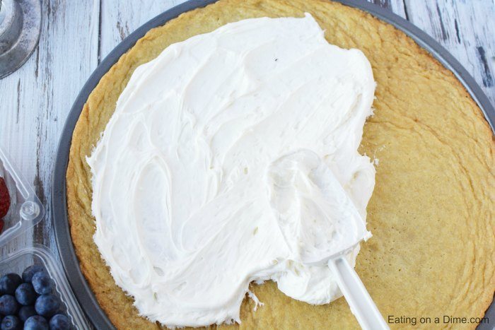 Close up image of cream cheese being spread on the sugar cookie crust. 