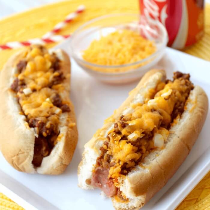 Chili Hot Dogs on a plate on a bowl of cheddar cheese 