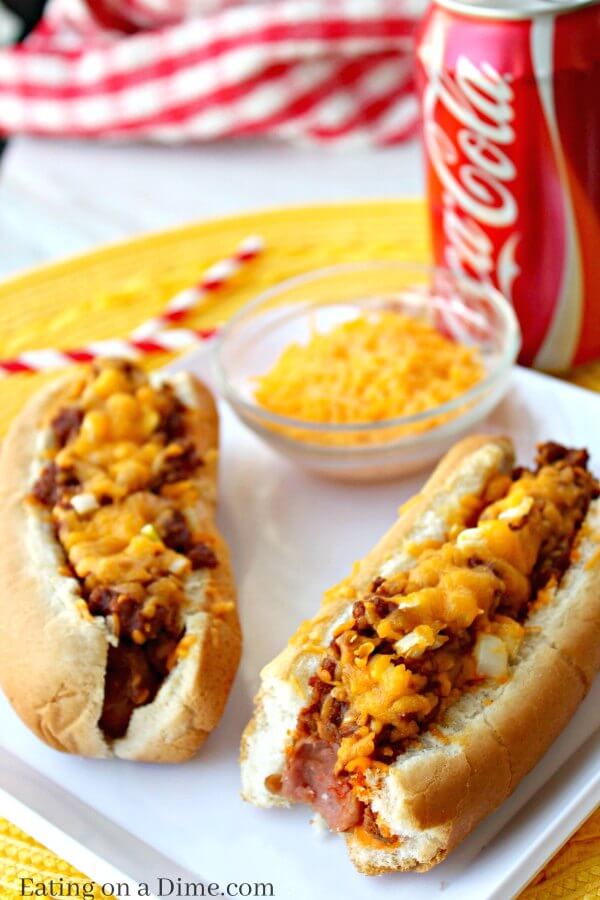 Chili Hot Dogs on a plate with a bowl of shredded cheese