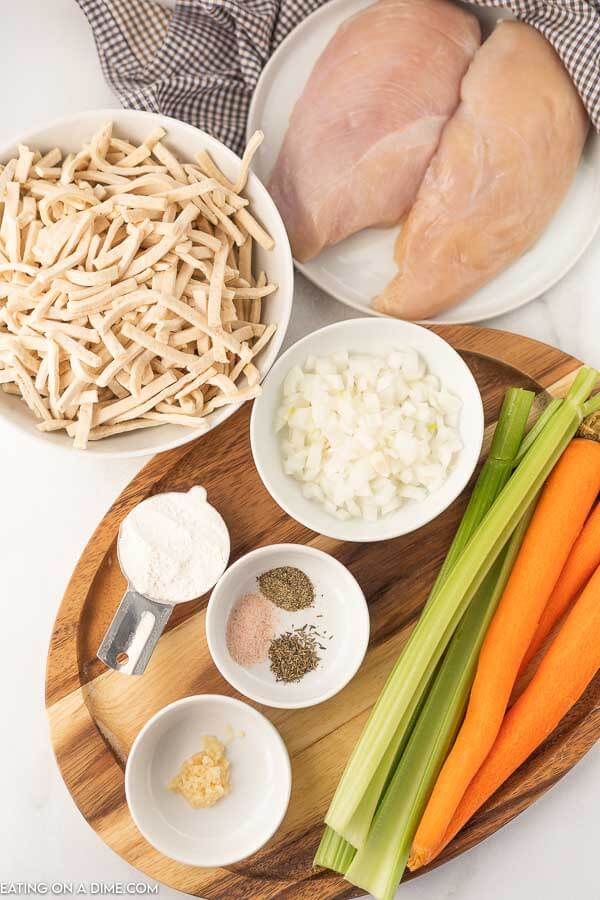 Close up of chicken breast, frozen noodles, onion, carrot, celery, and seasoning for Chicken Noodle soup on a table. 