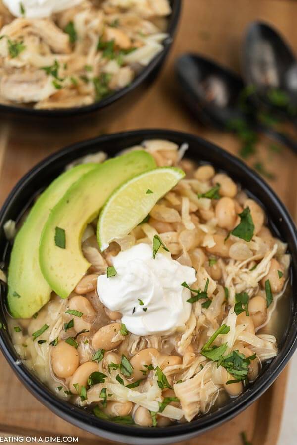 Close up image of a black bowl of white chicken chili with avocado, lime, and sour cream on a serving tray.