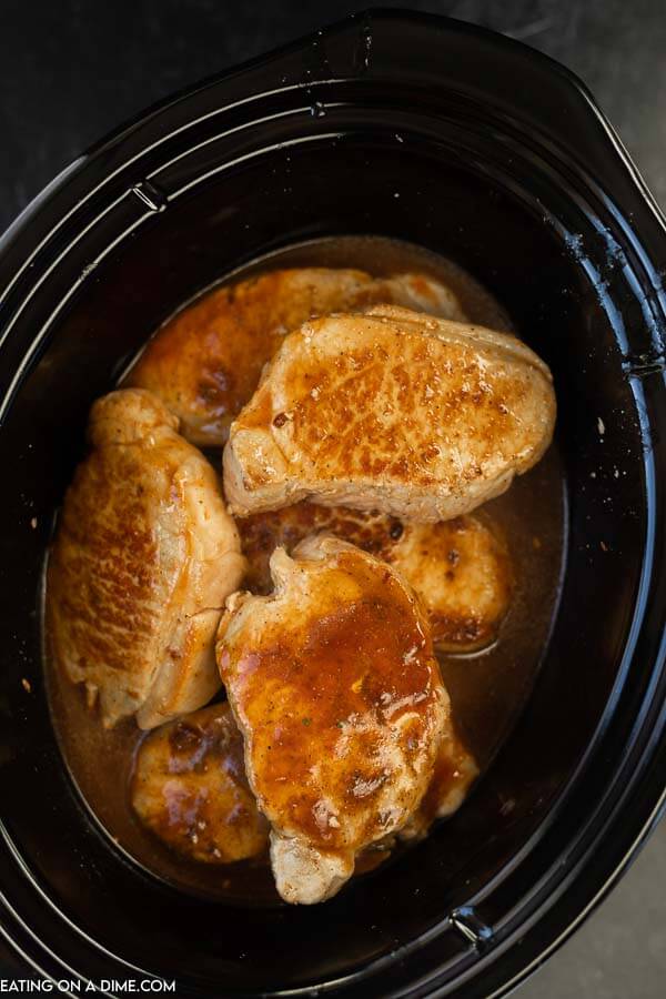 Browned pork chops in a crock pot with the other ingredients for this recipe 