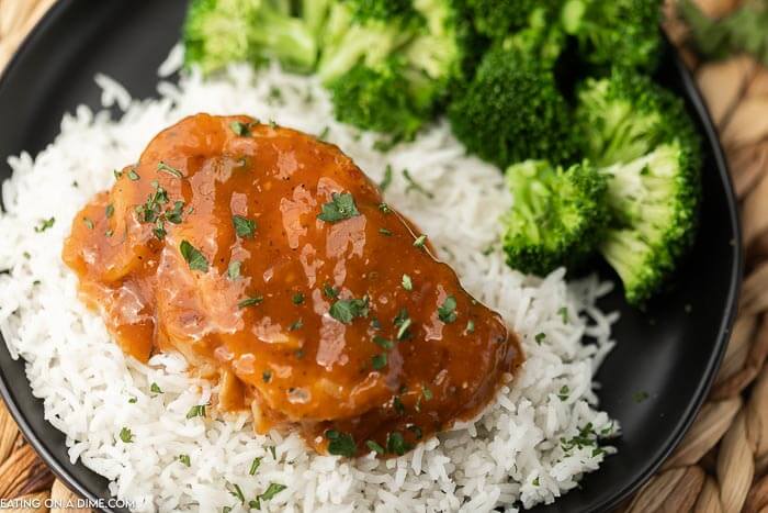 BBQ Pork chops over white rice topped with fresh parsley on a black plate with a side of broccoli 