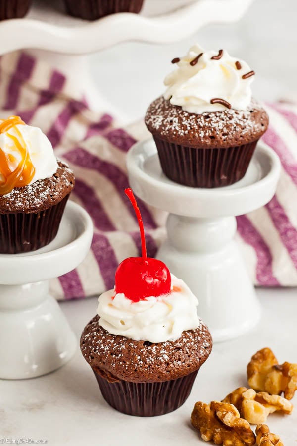 Close up image of brownie bites on a cake stand topped with cherry and caramel sauce.  