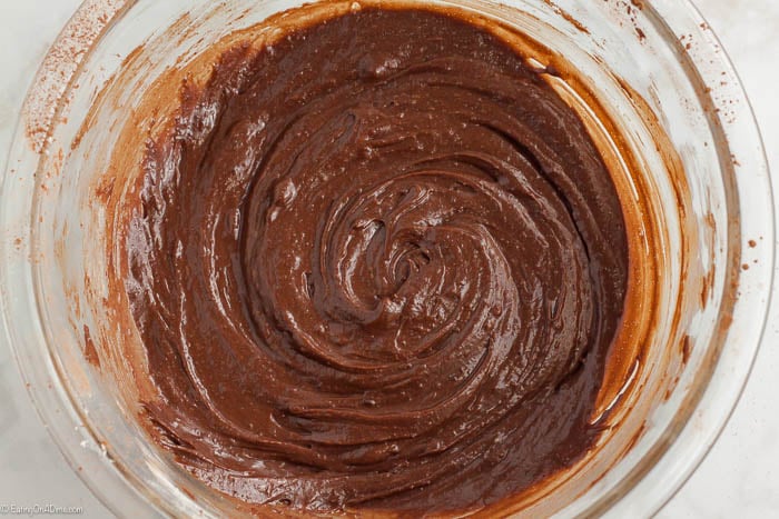 Close up image of brownie batter being mixed in a glass bowl. 