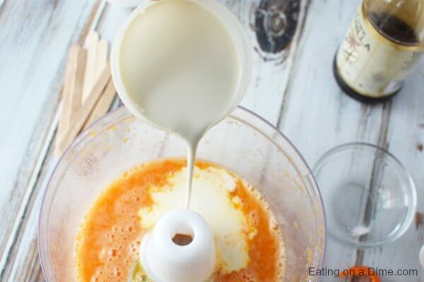 Close up image of heavy whipping cream being pour into the food processor with the other ingredients. 