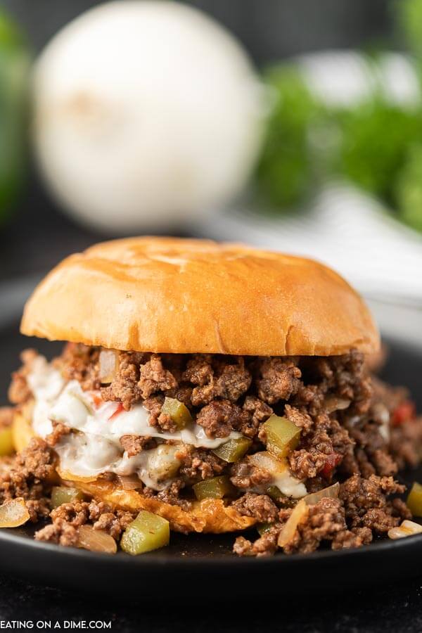 Philly Cheesesteak Sloppy Joes on a black plate with an onion and fresh parsley in the background 