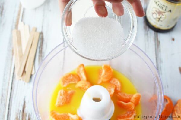 Sugar being poured into the food processor with the orange juice and oranges