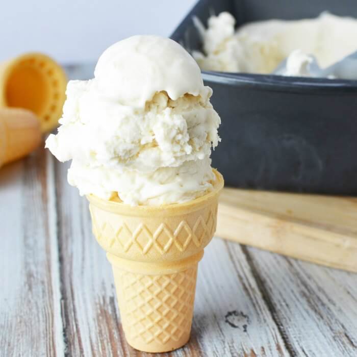 Homemade vanilla ice cream in a loaf pan with an ice cream scoop scooping out a portion of the ice cream.  