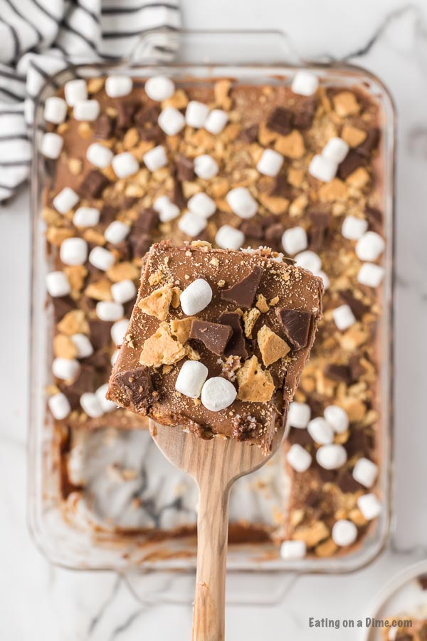 close up image of smores cake in a 9x13 pan with a serving on a wooden spoon. 