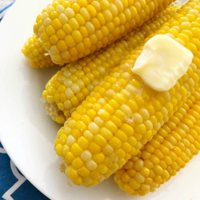 Close up image of corn on the cob on a white plate with melted butter. 