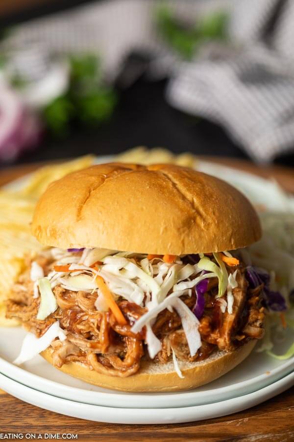 Pulled pork sandwich topped with slaw on a plate with potato chips. 