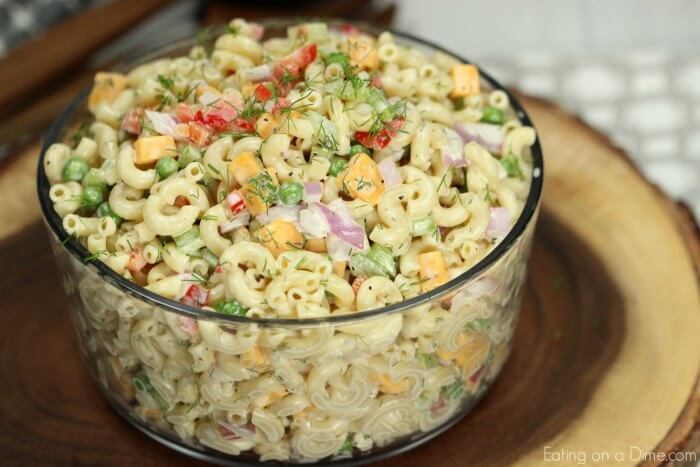 Creamy Macaroni Salad in a large bowl topped with fresh dill on a wooden platter 