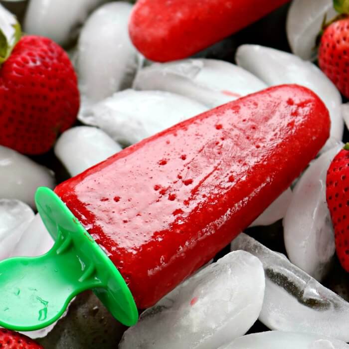 Close up image of strawberry popsicles on ice with fresh strawberries on the side. 