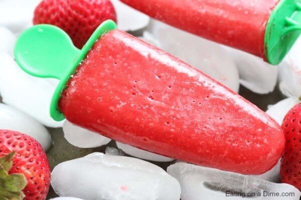 Close up image of strawberry popsicles on ice with strawberries on the side. 