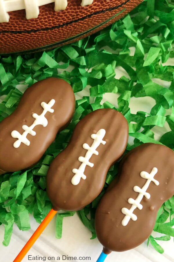 Close up image of three football cookie pops on green confetti. 