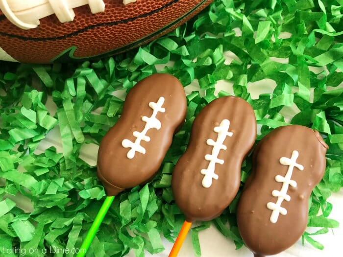 Close up image of three football cookie pops on green confetti with a football. 