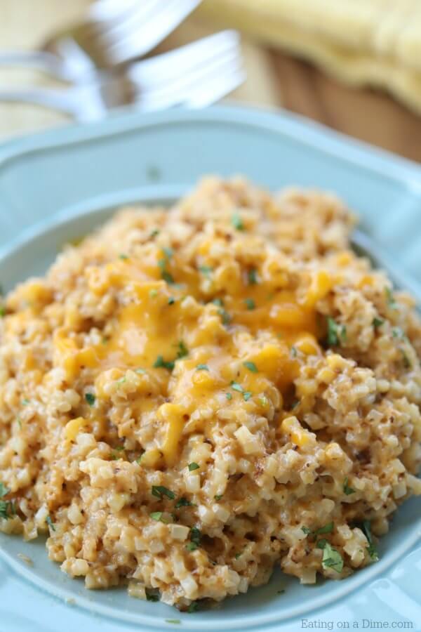 Close up image of cheesy cauliflower rice in a blue bowl topped with cheese. 