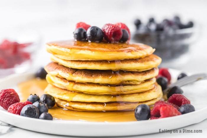 Close up image of prepared pancakes stacked on a plate with blueberries and raspberries. 