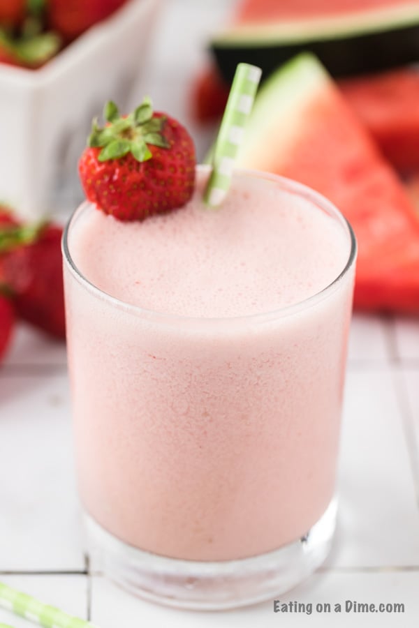 Close up image of a glass of watermelon strawberry smoothie with a whole strawberry and a straw. 