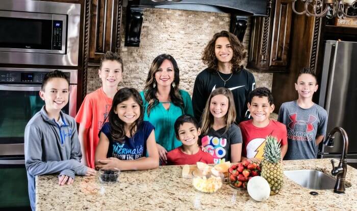 Carrie with her 8 kids standing in her kitchen with fresh fruit on the countertop 