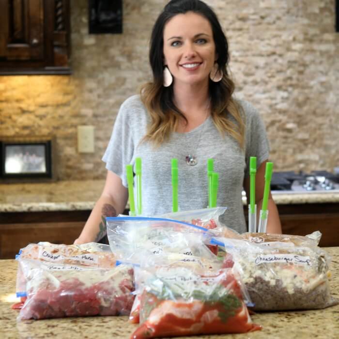 Carrie standing in her kitchen in front of some crock pot freezer meals with freezer bag holders on the counter as well 