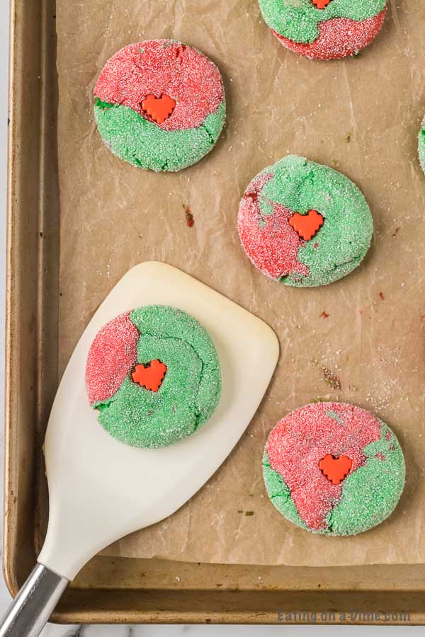 Close up image of Grinch cookies on a cookie sheet being served with a spatula. 