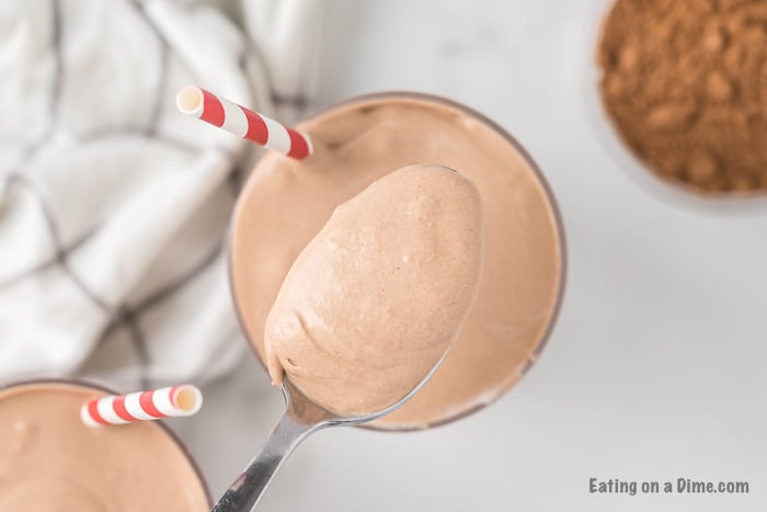 Close up image of chocolate shake in a glass with a red and white stripe straw.