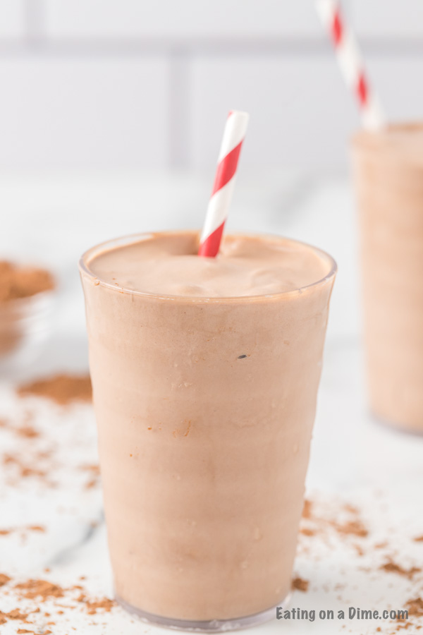 Close up image of chocolate shake in a glass with a red and white stripe straw. 