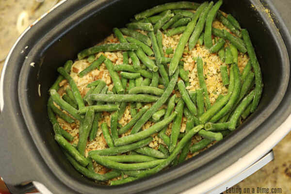 Adding the frozen green beans in the slow cooker on top of the stuffing