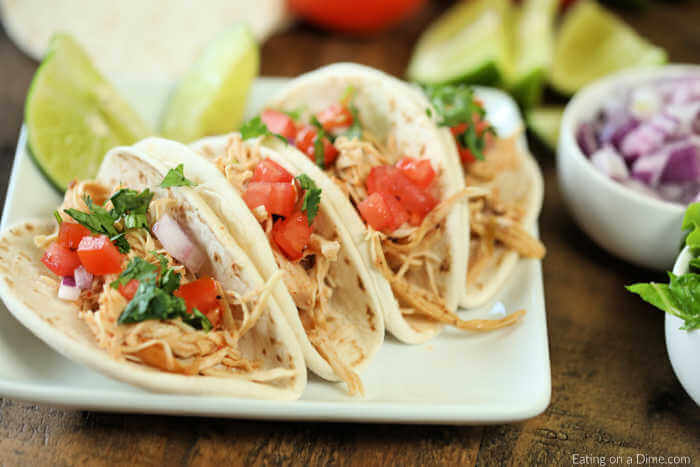 Close up image of chicken ranch tacos on a white platter with a side of red onion and tomatoes and lettuce.