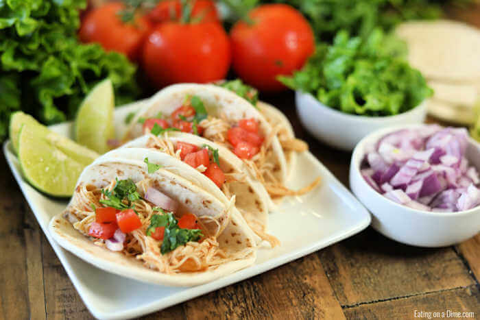 Close up image of chicken ranch tacos on a white platter with a side of red onion and tomatoes and lettuce.