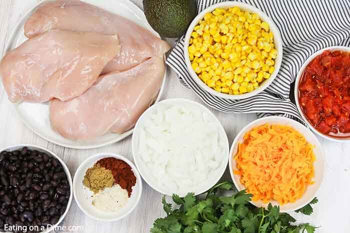 Close up image of ingredients for chicken tortilla soup - chicken breast, black beans, spices, onion, cheese, diced tomatoes, corn, avocado and cilantro. 