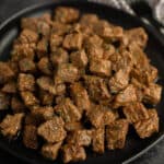 Close up image of steak bites on a black plate.