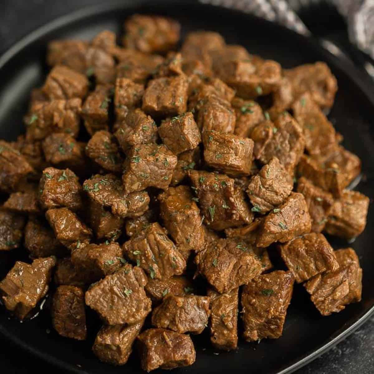 Close up image of steak bites on a black plate.