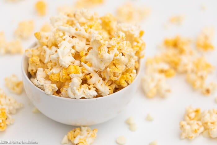 A bowl full of white chocolate popcorn with popcorn scattered around it as well. 