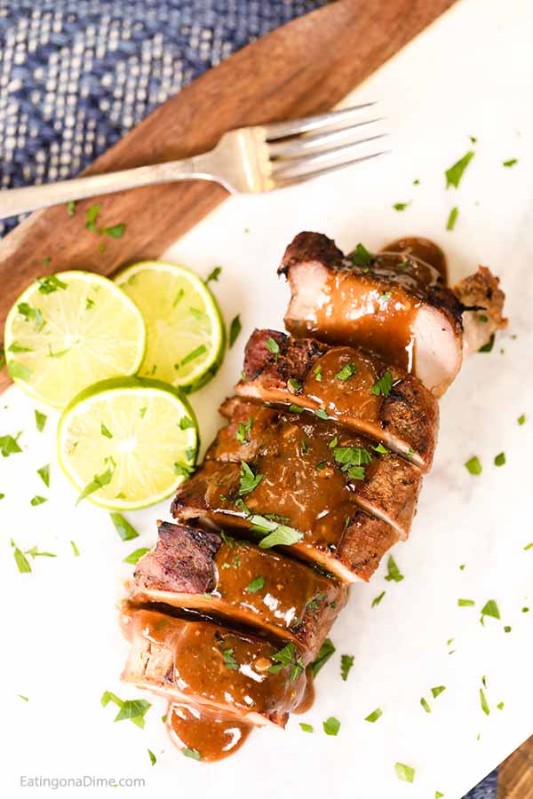Sliced Pork Tenderloin topped with a honey lime sauce with sliced limes next to it.  