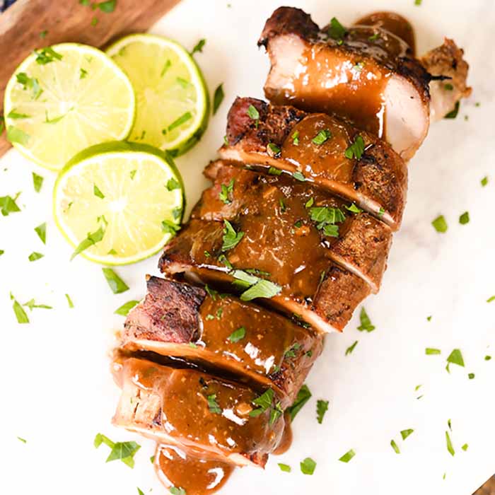 Sliced Pork Tenderloin topped with a honey lime sauce with sliced limes next to it and topped with fresh cilantro. 