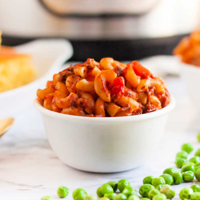 Goulash in a white bowl with a side of green peas. 