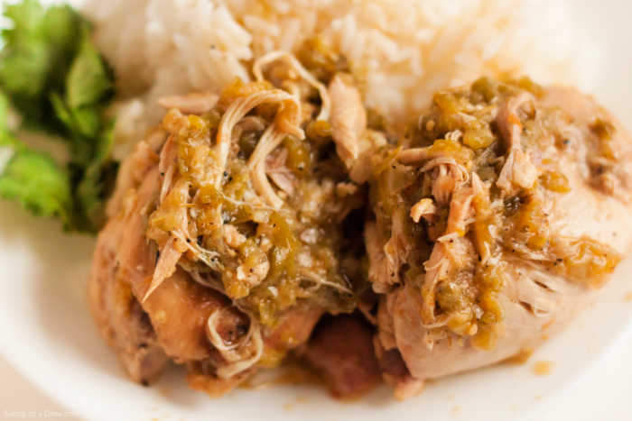 Close up image of salsa verde chicken on a white plate with a side of rice and broccoli