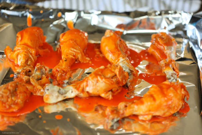Broiling chicken drumsticks on a cookie sheet with extra buffalo sauce