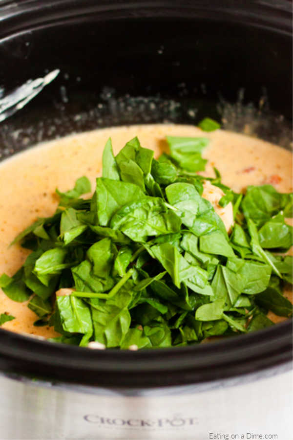 Close up image of creamy tuscan chicken in process of adding spinach. 