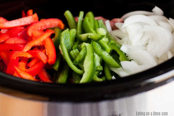 Ingredients needed for philly cheesesteaks - red bell pepper, green bell pepper, onion in the crock pot. 