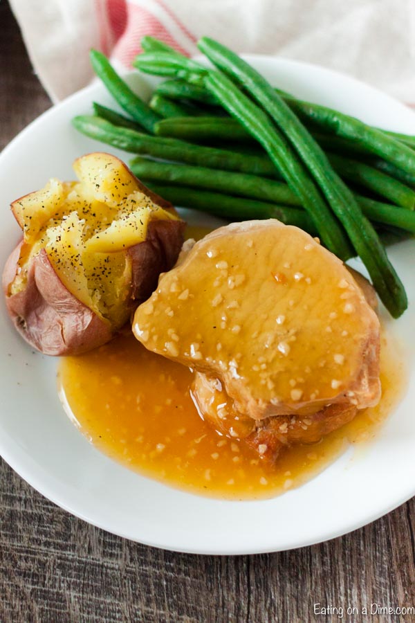 Close up image of honey garlic pork chops on a plate with a bake potato and a side of green beans. 